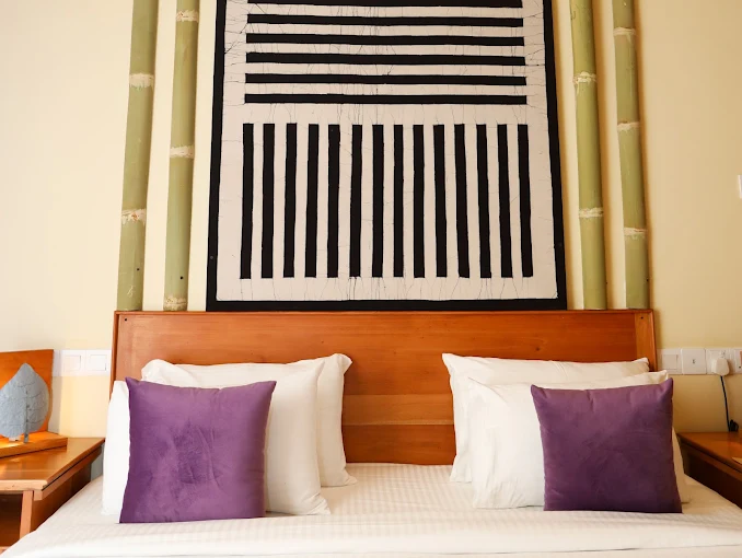 Guest room bed with batik wall art and purple accents at The Feel Hotel Ella